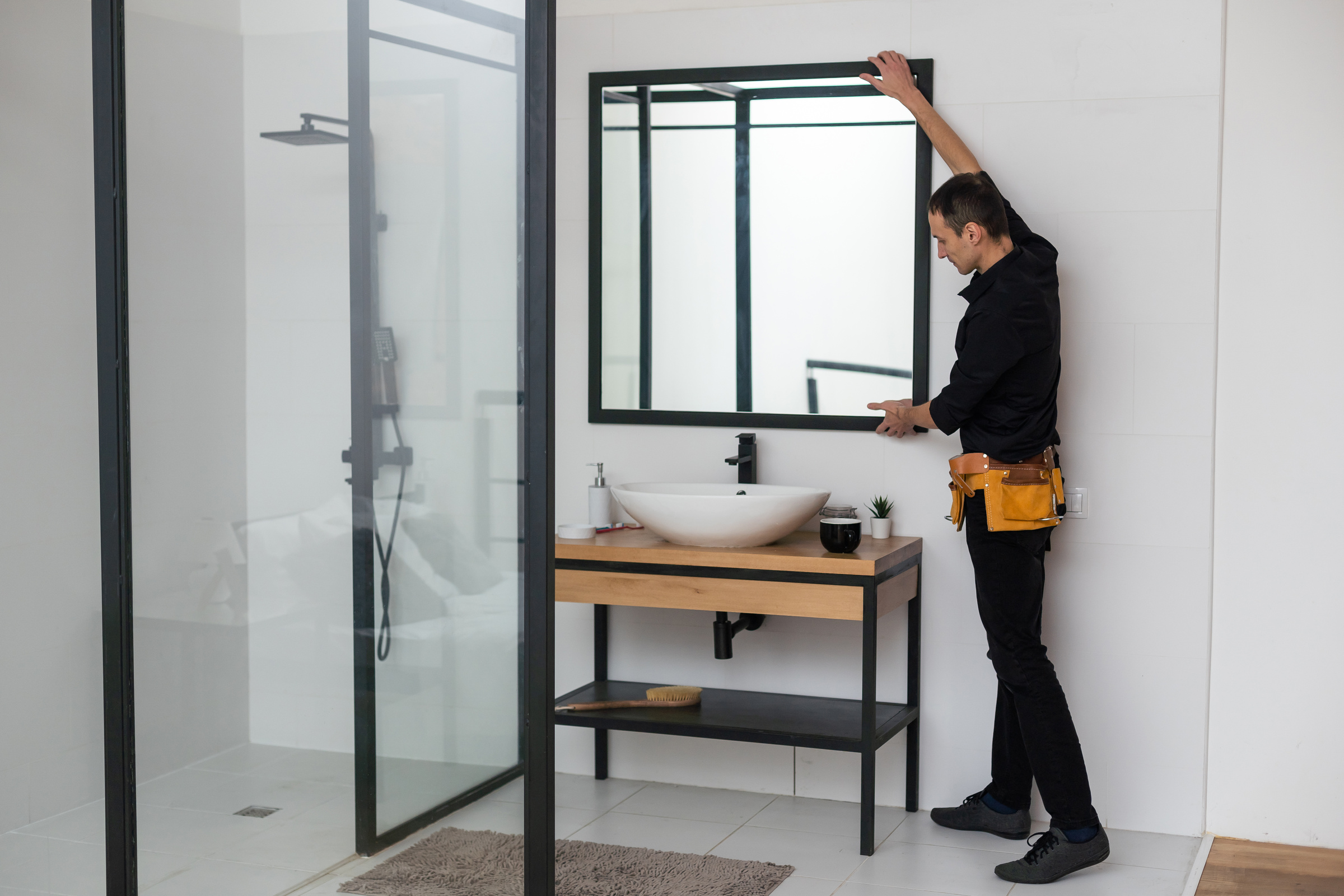 The worker installs the mirror in the bathroom.